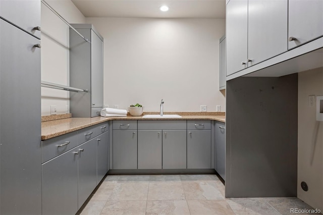 kitchen with recessed lighting, a sink, light stone countertops, and gray cabinetry