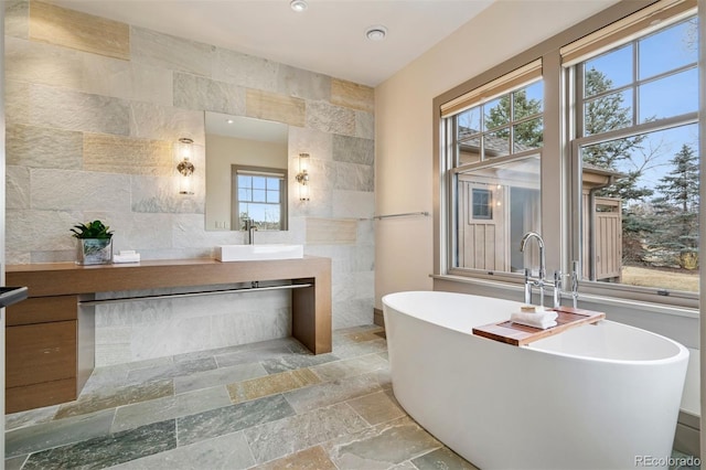 full bathroom featuring a freestanding tub, tile walls, stone tile flooring, and vanity