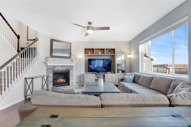 living room with ceiling fan, wood-type flooring, and a stone fireplace