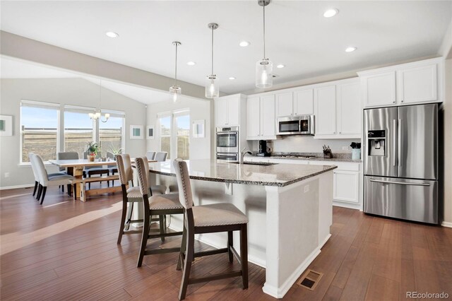 kitchen with decorative light fixtures, white cabinetry, stainless steel appliances, a kitchen island with sink, and vaulted ceiling