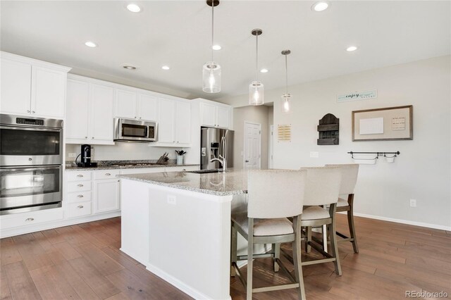 kitchen with hanging light fixtures, white cabinets, an island with sink, stainless steel appliances, and a breakfast bar area