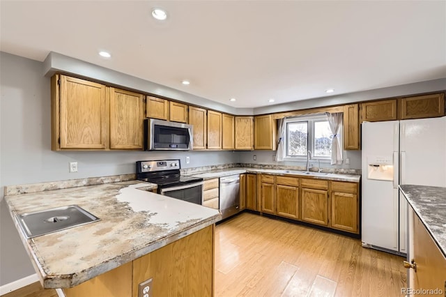kitchen featuring recessed lighting, light wood finished floors, a sink, a peninsula, and appliances with stainless steel finishes