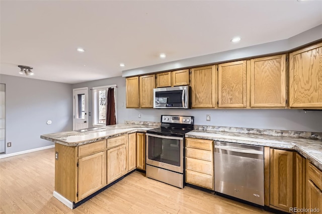 kitchen with light countertops, light wood finished floors, a peninsula, and appliances with stainless steel finishes