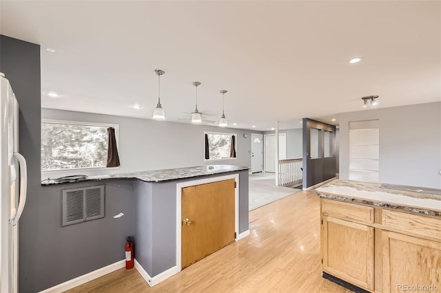 kitchen with light stone counters, light wood finished floors, visible vents, and decorative light fixtures