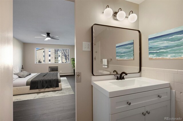 bathroom with an AC wall unit, hardwood / wood-style floors, a baseboard radiator, vanity, and ceiling fan