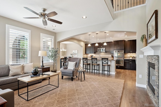 9528 Pendio Ct, Highlands Ranch, CO 80126 - living area with arched walkways, ceiling fan, light wood-style floors, recessed lighting, and a stone fireplace