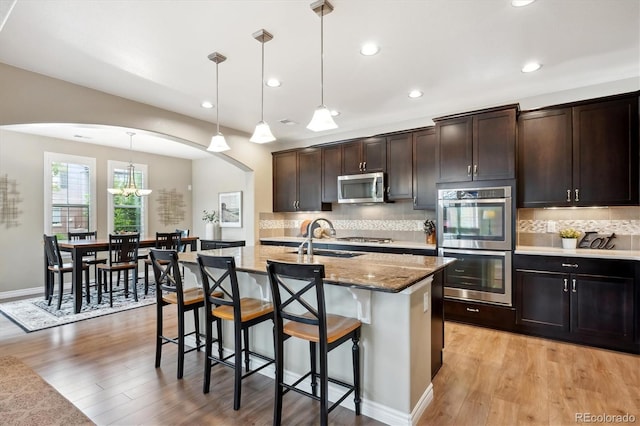 9528 Pendio Ct, Highlands Ranch, CO 80126 - kitchen featuring stainless steel appliances, a sink, arched walkways, a kitchen bar, and light stone countertops