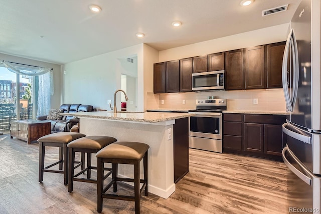 kitchen featuring appliances with stainless steel finishes, a kitchen island with sink, light hardwood / wood-style flooring, a breakfast bar, and sink