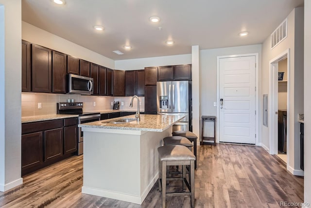 kitchen with a breakfast bar, sink, light stone countertops, an island with sink, and stainless steel appliances