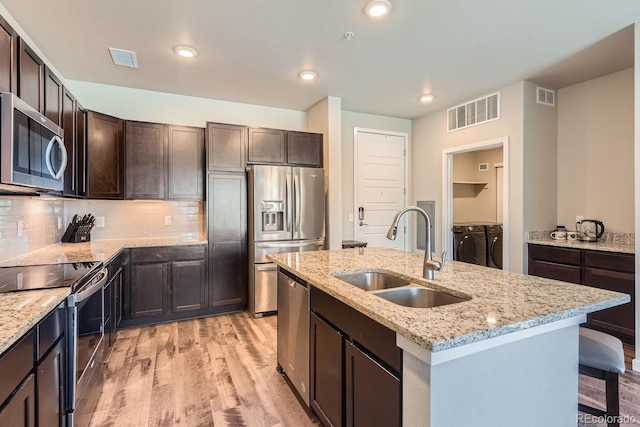 kitchen with an island with sink, stainless steel appliances, washer and dryer, light hardwood / wood-style flooring, and sink