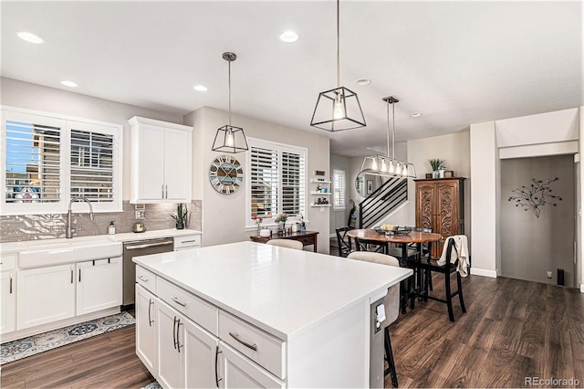 kitchen featuring sink, dishwasher, white cabinets, a kitchen island, and decorative light fixtures