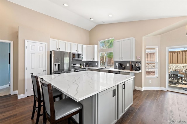 2209 Lupine Pl, Erie, CO 80516 - kitchen featuring appliances with stainless steel finishes, light stone countertops, high vaulted ceiling, decorative backsplash, and a kitchen bar