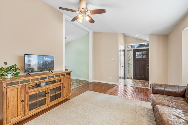 living room featuring ceiling fan, vaulted ceiling, baseboards, and wood finished floors