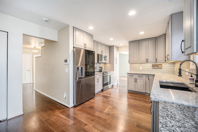 kitchen featuring light stone countertops, appliances with stainless steel finishes, backsplash, sink, and gray cabinets