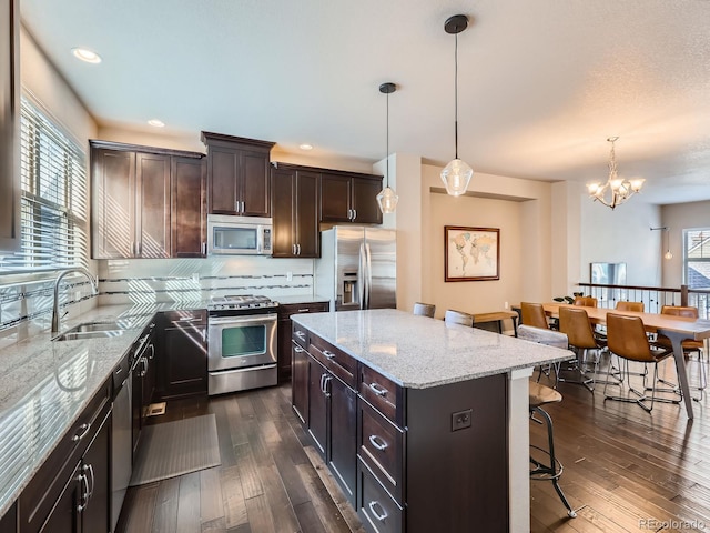 kitchen featuring sink, hanging light fixtures, appliances with stainless steel finishes, a kitchen island, and dark hardwood / wood-style flooring