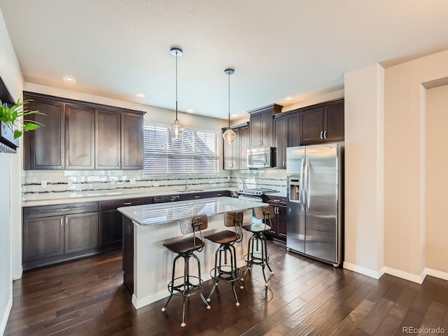 kitchen featuring dark hardwood / wood-style floors, a kitchen island, hanging light fixtures, and appliances with stainless steel finishes