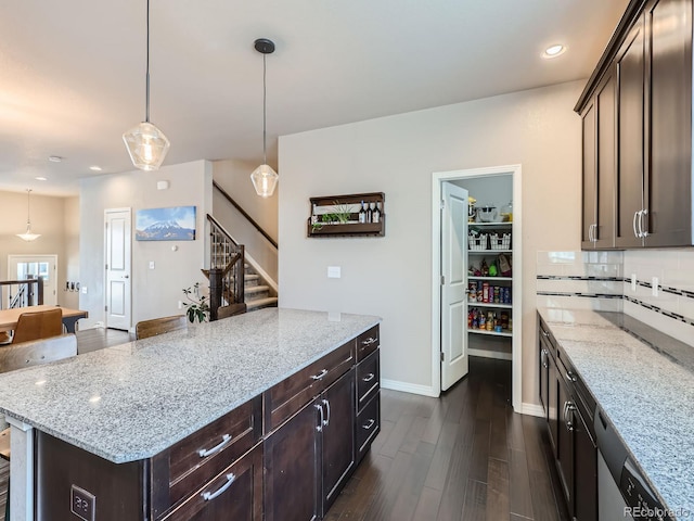 kitchen with decorative backsplash, pendant lighting, light stone counters, and dark wood-type flooring