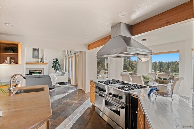 kitchen with island exhaust hood, stainless steel range, a textured ceiling, sink, and beam ceiling