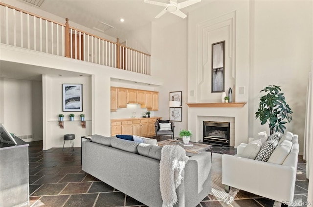 living room featuring ceiling fan, a towering ceiling, and a tile fireplace