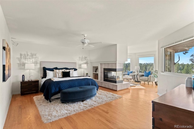 bedroom featuring ceiling fan, light hardwood / wood-style floors, and a tile fireplace