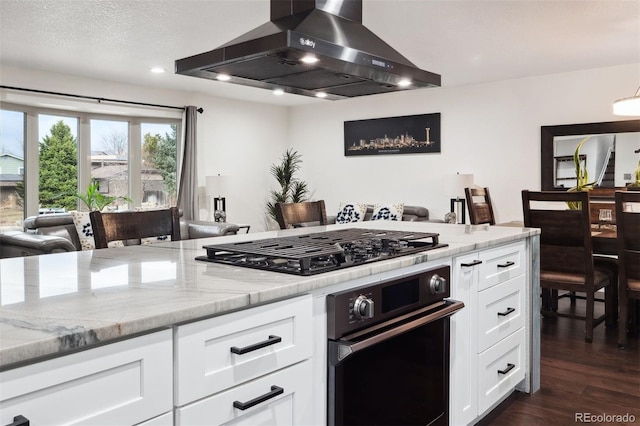 kitchen with light stone counters, dark wood-style flooring, white cabinets, wall chimney range hood, and black appliances