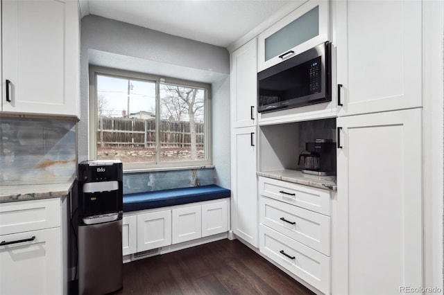 kitchen featuring white cabinetry, black microwave, light stone counters, and dark wood-type flooring