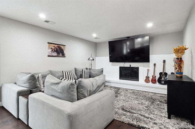 living room with a glass covered fireplace, visible vents, dark wood finished floors, and recessed lighting