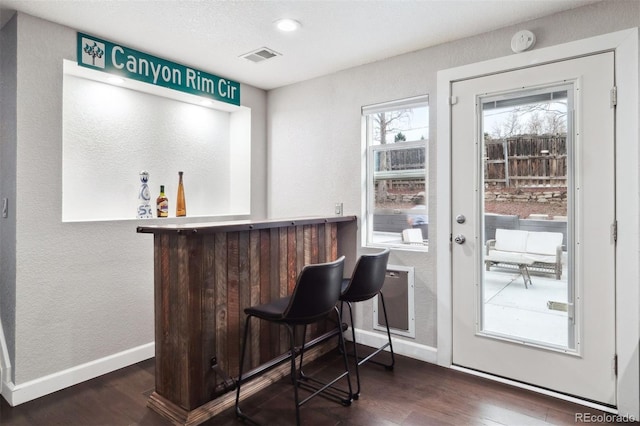 bar with a dry bar, baseboards, visible vents, and wood finished floors