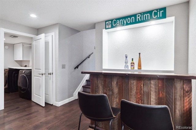 bar featuring visible vents, dark wood-type flooring, washing machine and dryer, a bar, and baseboards