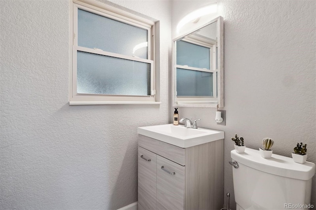 half bath with toilet, vanity, and a textured wall