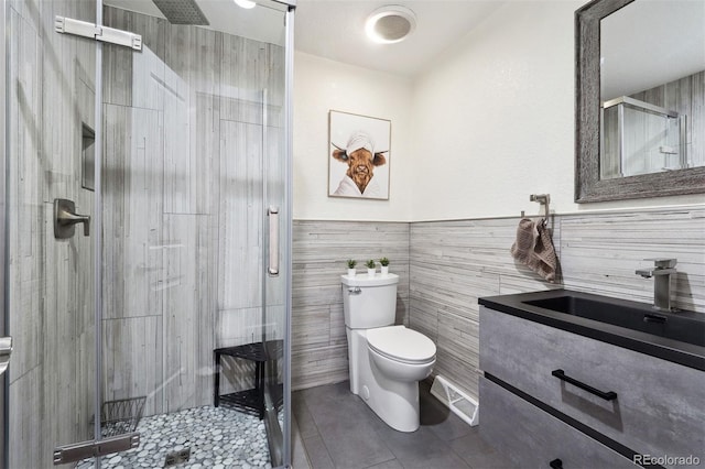 full bath with a stall shower, toilet, tile patterned flooring, vanity, and tile walls