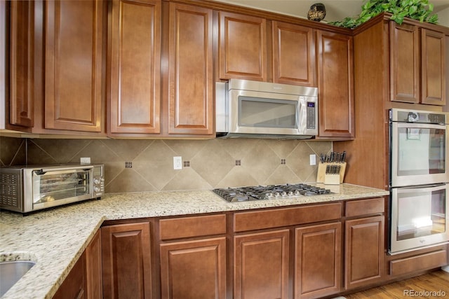2033 E 167th Way, Thornton, CO 80602 - kitchen featuring stainless steel appliances, light stone counters, brown cabinets, and tasteful backsplash
