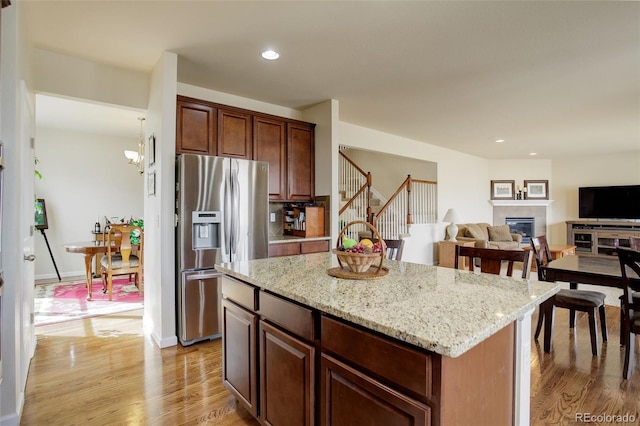 2033 E 167th Way, Thornton, CO 80602 - kitchen with stainless steel fridge, light wood-style floors, a tiled fireplace, a kitchen island, and recessed lighting