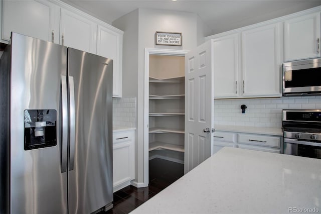 kitchen with white cabinetry, dark hardwood / wood-style floors, stainless steel appliances, light stone countertops, and backsplash