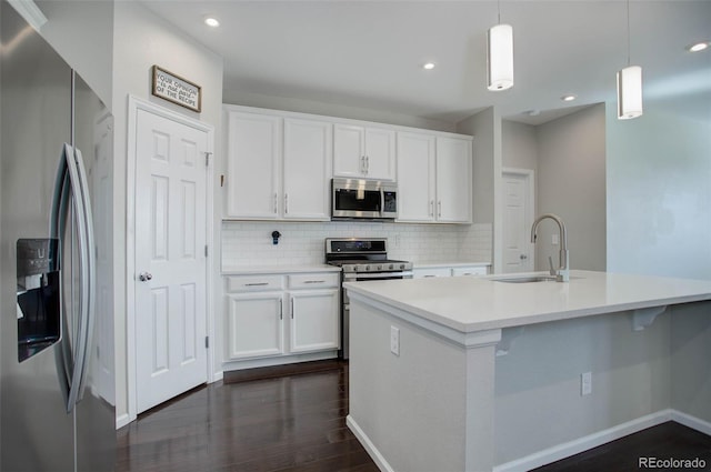 kitchen featuring white cabinetry, appliances with stainless steel finishes, hanging light fixtures, and a center island with sink