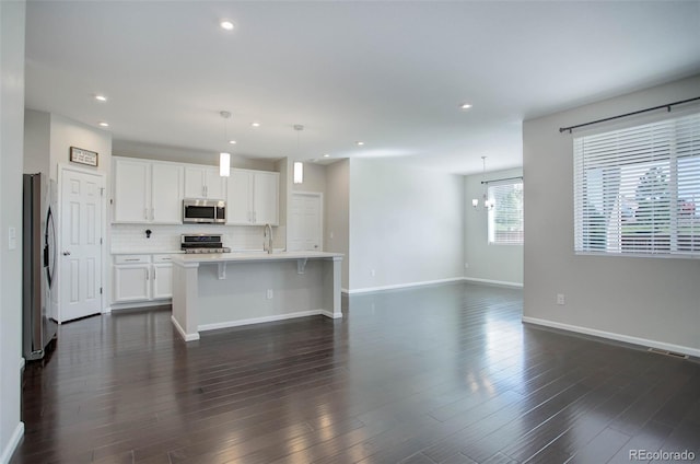 kitchen with white cabinetry, hanging light fixtures, a center island with sink, appliances with stainless steel finishes, and decorative backsplash