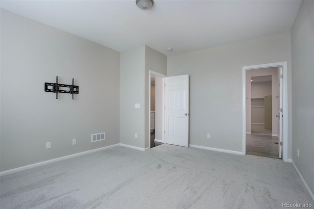 unfurnished bedroom with light carpet and a walk in closet