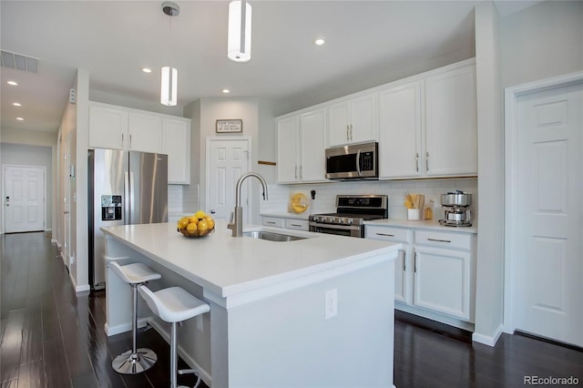 kitchen featuring dark wood finished floors, an island with sink, a sink, appliances with stainless steel finishes, and tasteful backsplash