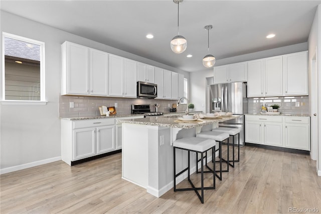 18815 W 93rd Ave, Arvada, CO 80007 - kitchen featuring appliances with stainless steel finishes, decorative backsplash, white cabinets, a kitchen bar, and light wood-type flooring