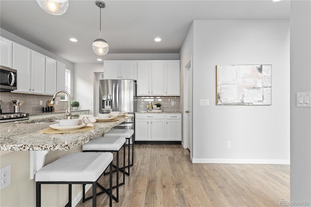 18815 W 93rd Ave, Arvada, CO 80007 - kitchen with stainless steel appliances, tasteful backsplash, a breakfast bar area, light stone countertops, and white cabinets