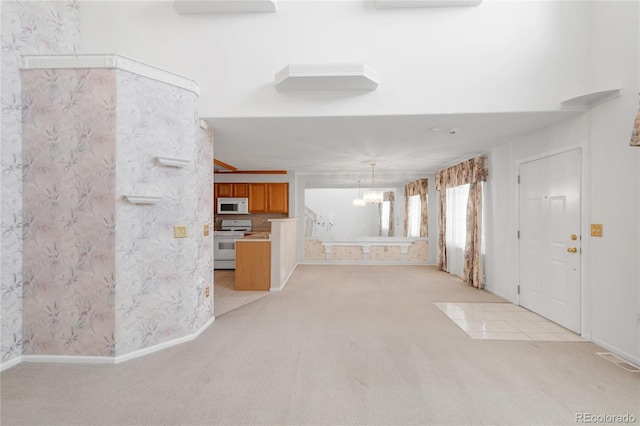 unfurnished living room featuring visible vents, baseboards, wallpapered walls, a notable chandelier, and light colored carpet