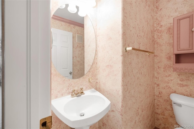 bathroom with visible vents, toilet, a sink, crown molding, and wallpapered walls