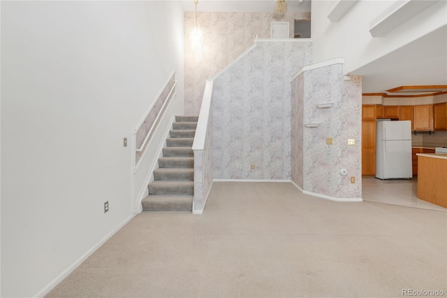 stairs with wallpapered walls, carpet, baseboards, and a towering ceiling