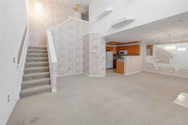 unfurnished living room featuring wallpapered walls, stairway, light carpet, a high ceiling, and a notable chandelier