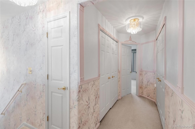 hallway featuring light carpet, a chandelier, wainscoting, and wallpapered walls