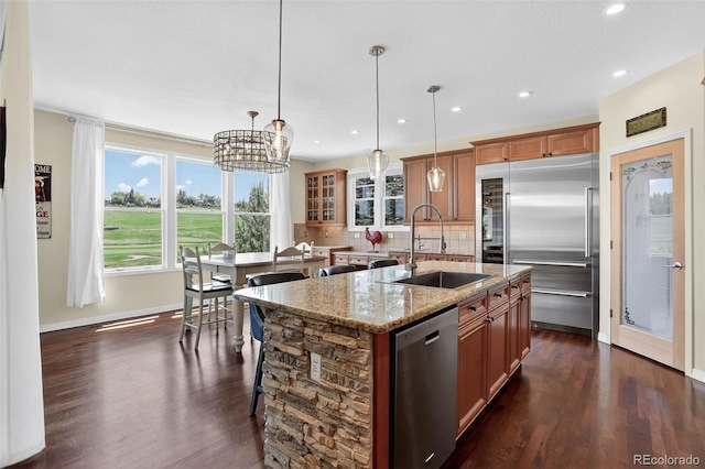 11208 W Ontario Ave, Littleton, CO 80127 - kitchen featuring stainless steel appliances, brown cabinets, dark wood-style floors, light stone counters, and decorative backsplash