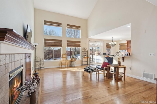 living room featuring a high ceiling, a notable chandelier, light wood-type flooring, and a fireplace