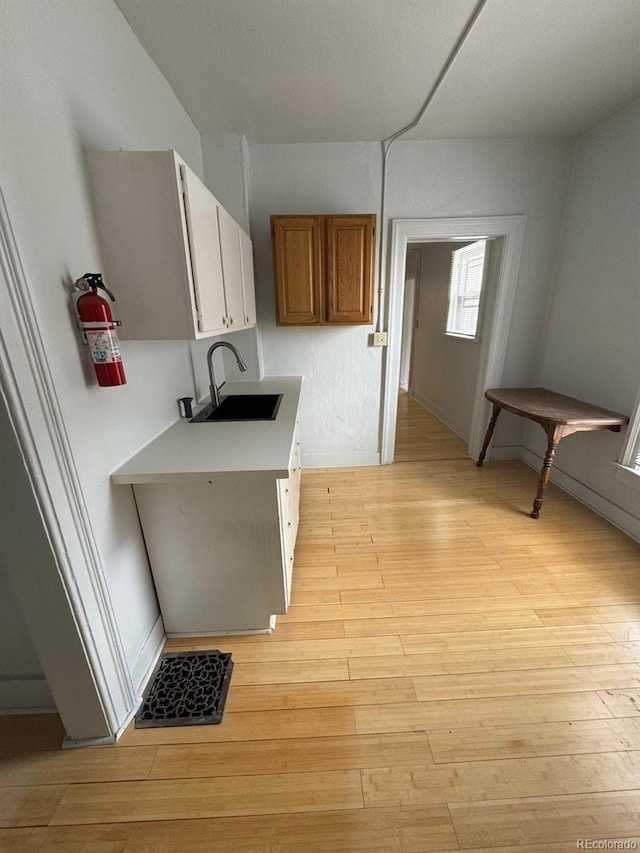 kitchen with brown cabinets, light wood finished floors, light countertops, white cabinets, and a sink