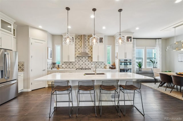 kitchen featuring a kitchen island with sink, white cabinetry, stainless steel appliances, and wall chimney exhaust hood