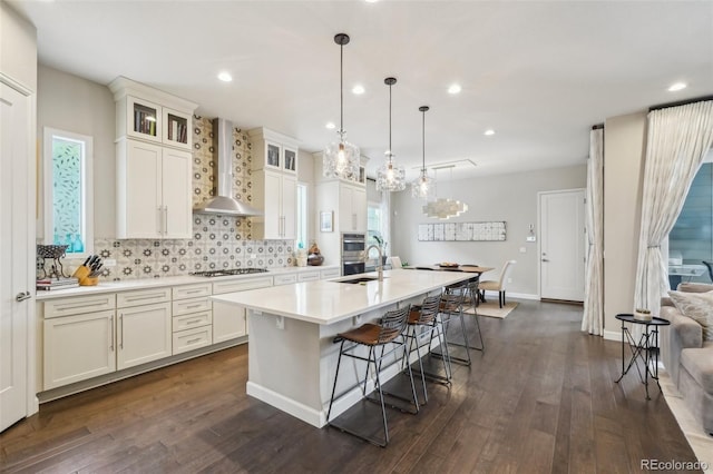 kitchen featuring tasteful backsplash, gas stovetop, wall chimney range hood, light countertops, and a center island with sink